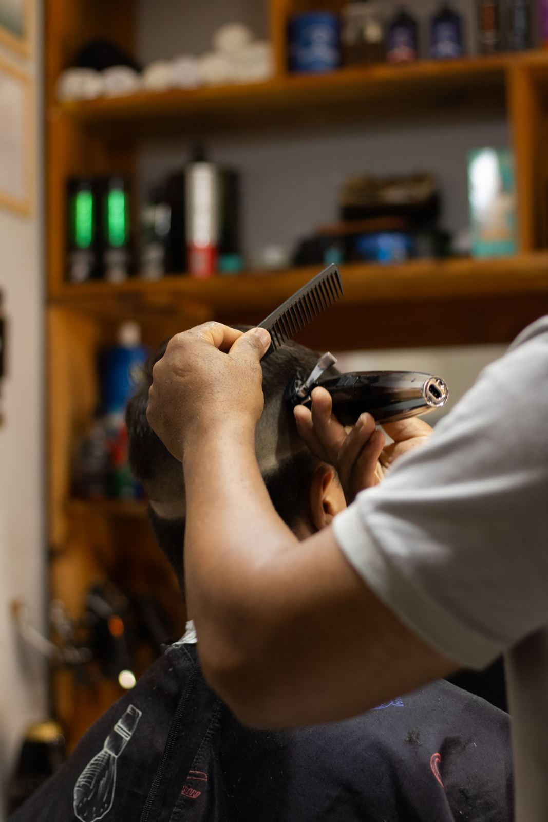 Barber lining up a client's cut in front of a wall of grooming products