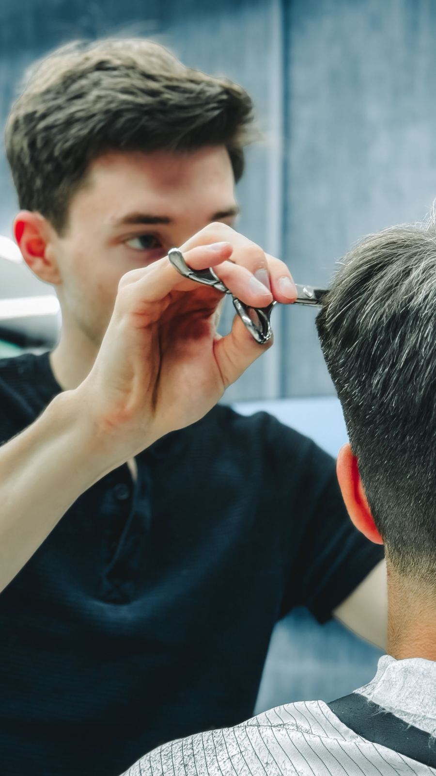 Young barber carefully scissor-cutting a client's hair