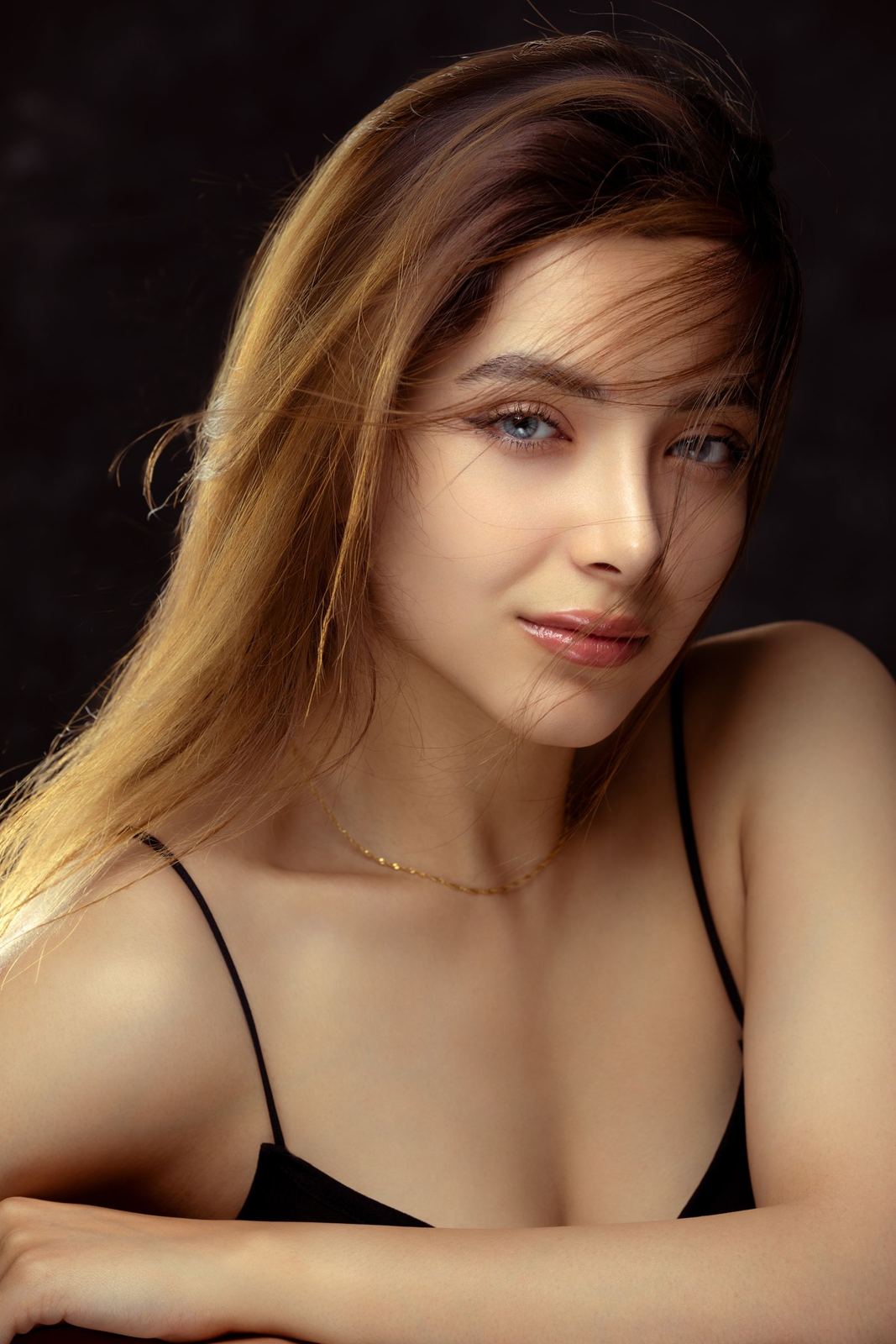 Woman with golden-blonde balayage against a dark backdrop