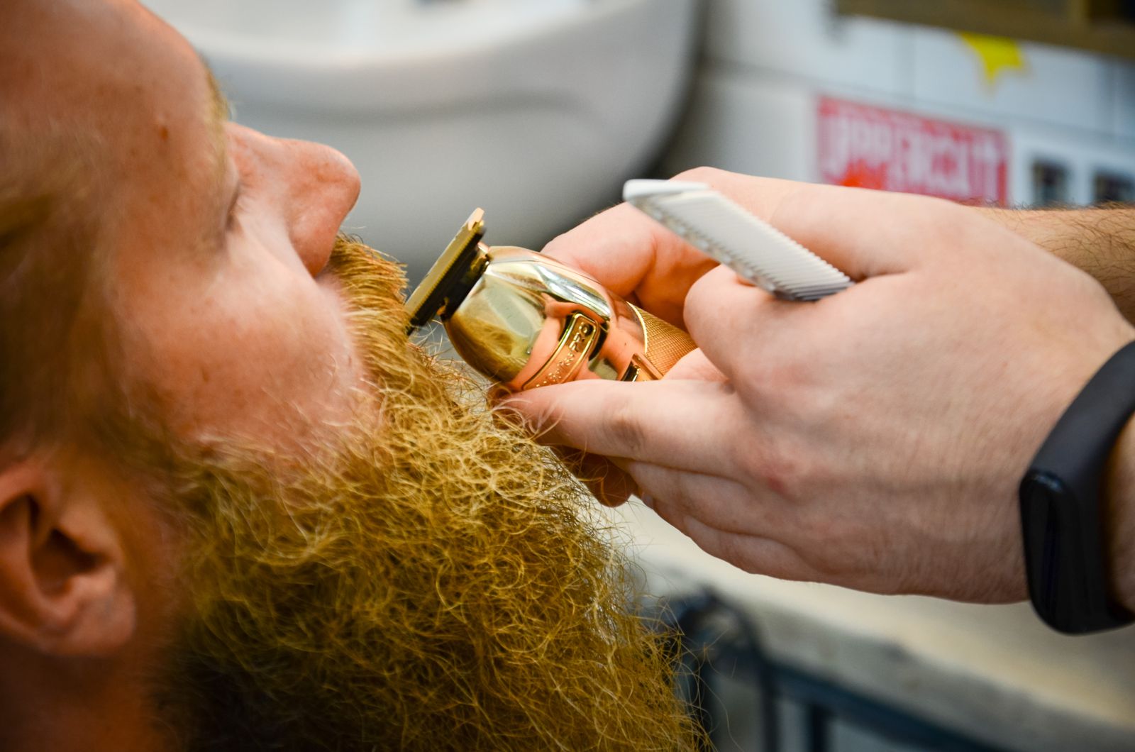 Close-up of a gold trimmer shaping a red beard