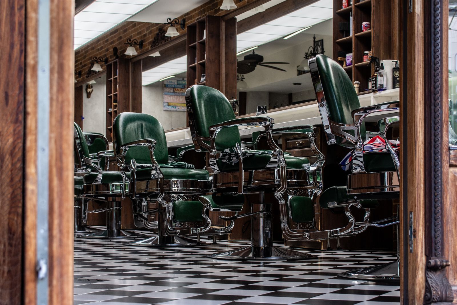 A row of green leather barber chairs on a black-and-white checkered floor