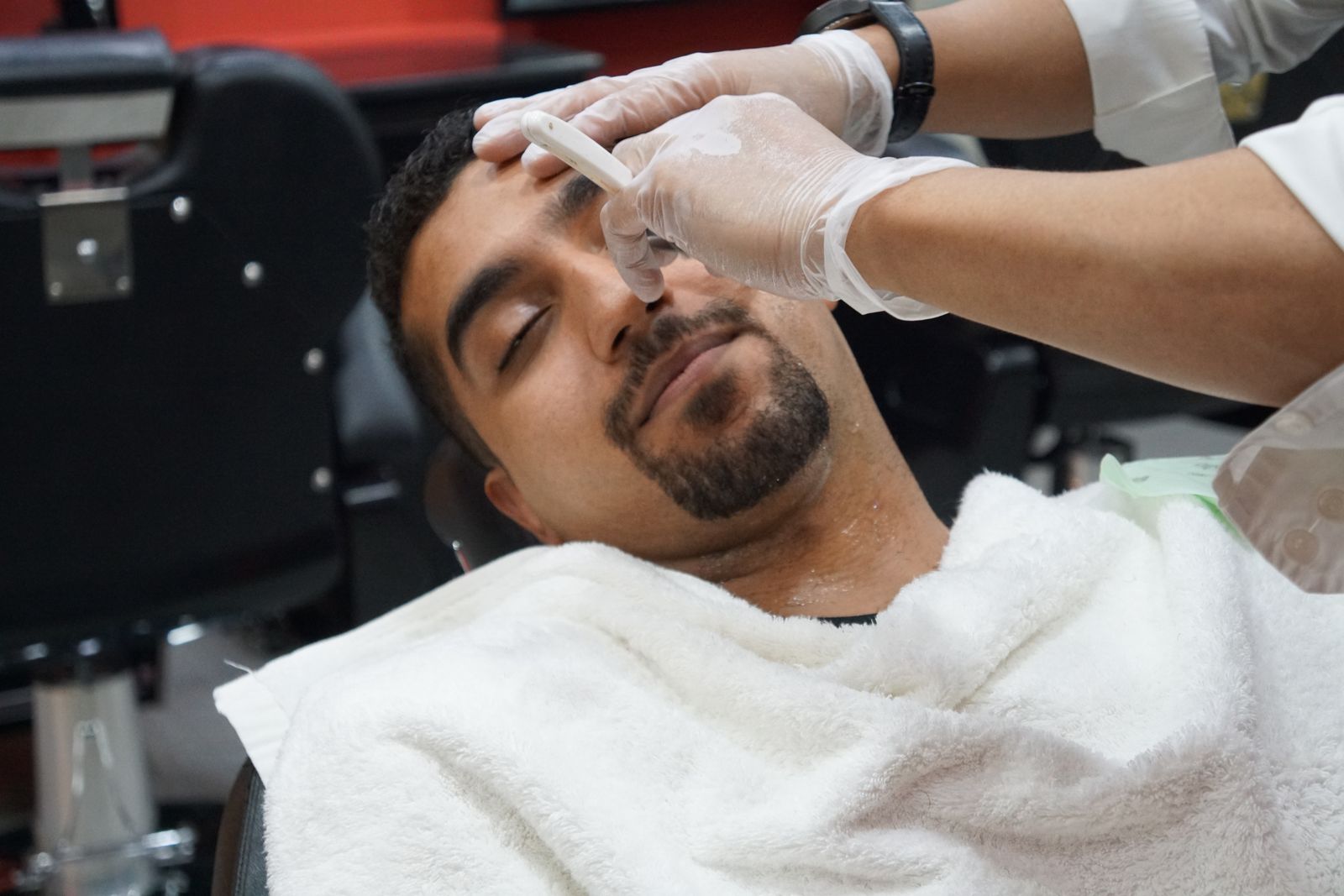 Client reclined under a white towel before a shave