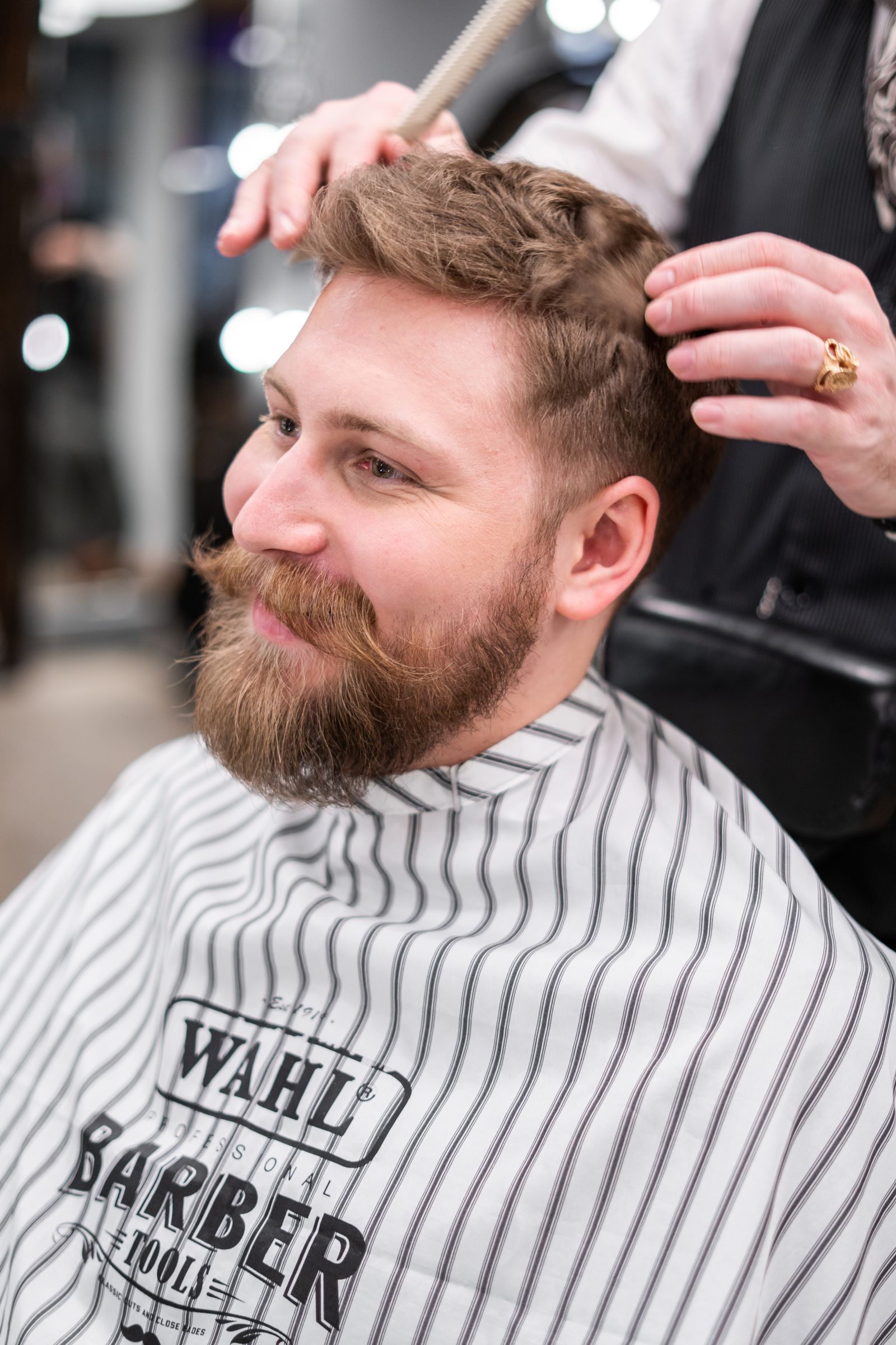 Smiling bearded client in a striped barber cape