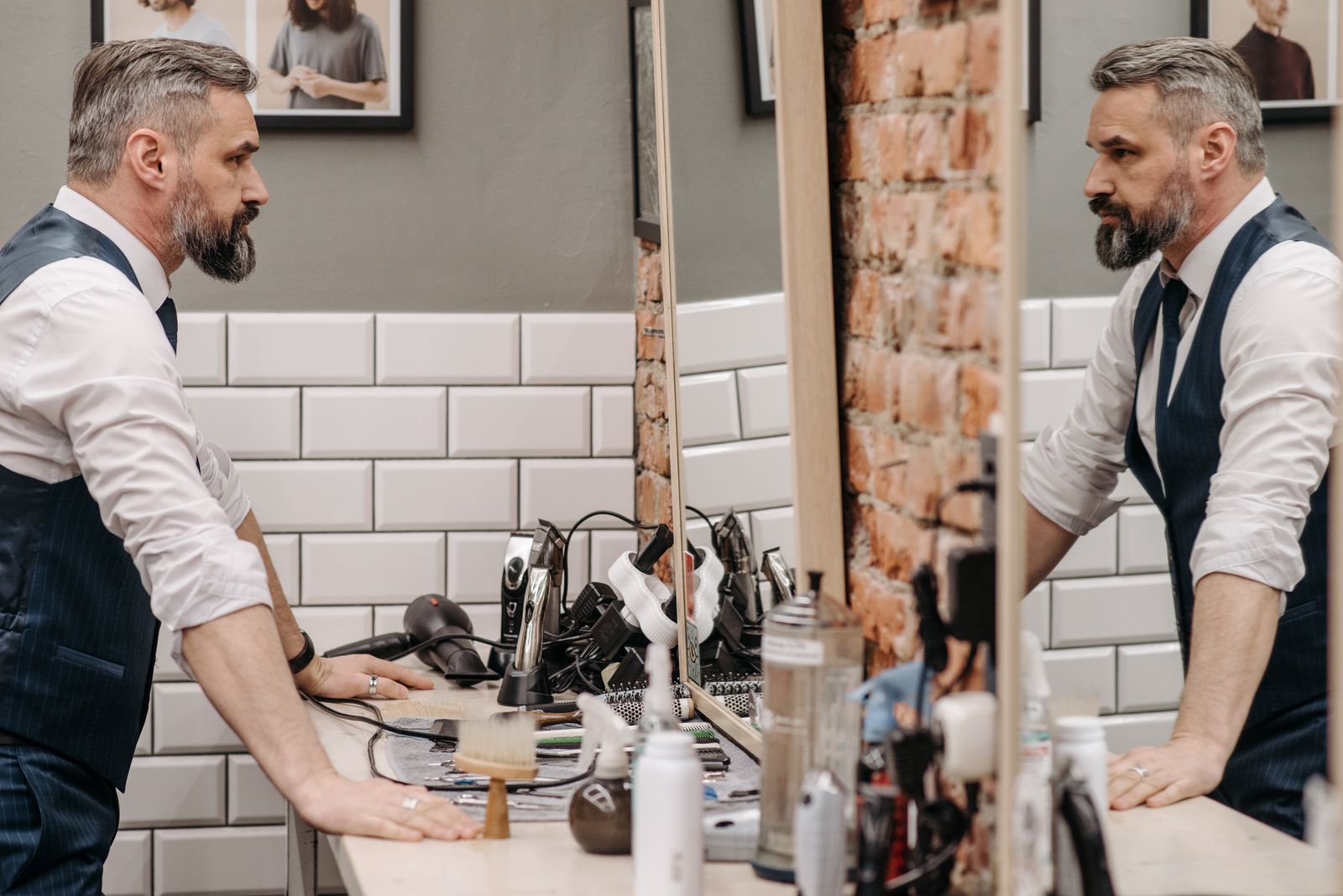 A silver-bearded barber in a pinstripe waistcoat and tie at his station mirror