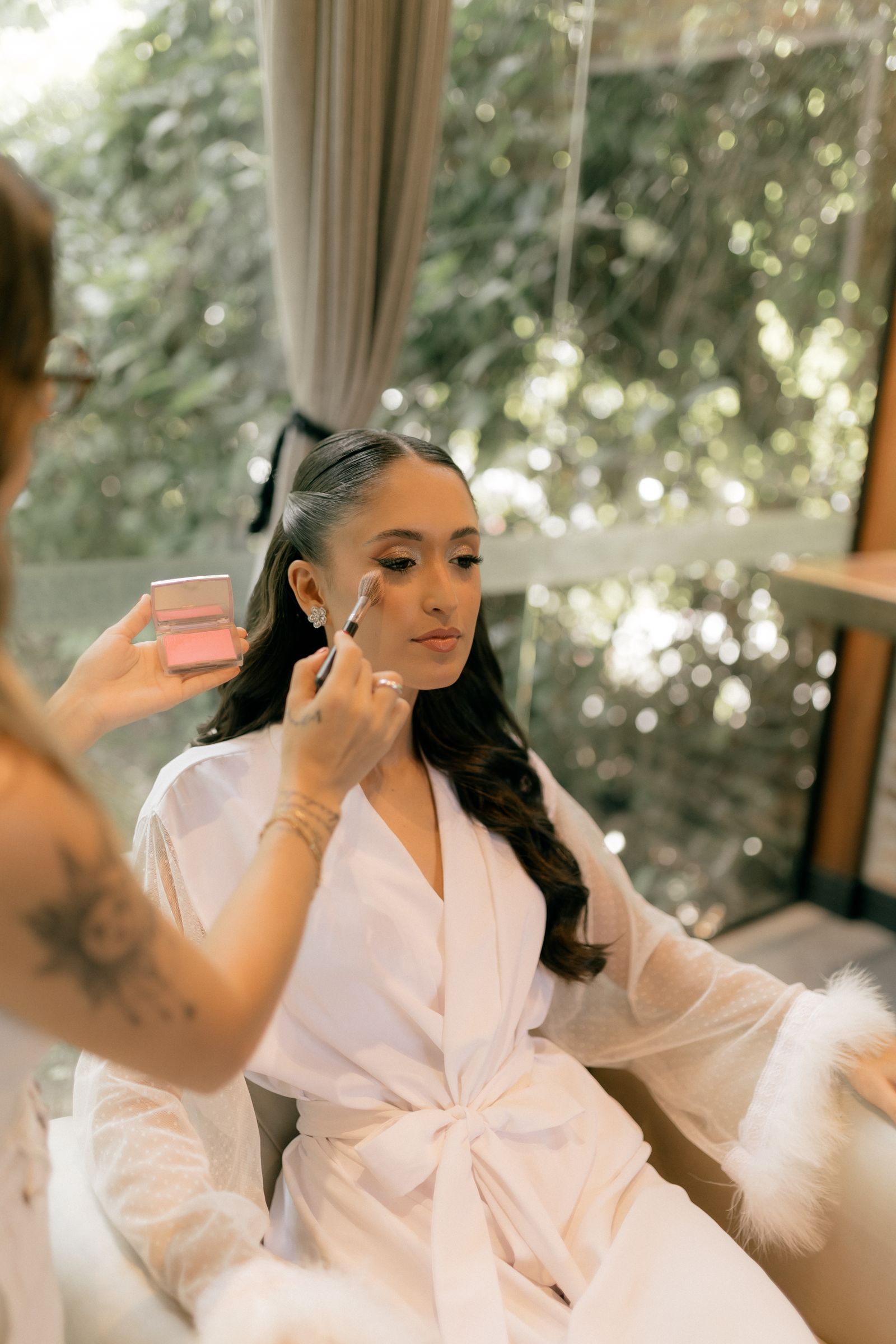 Bride in a blush robe having her makeup applied on the morning of her wedding