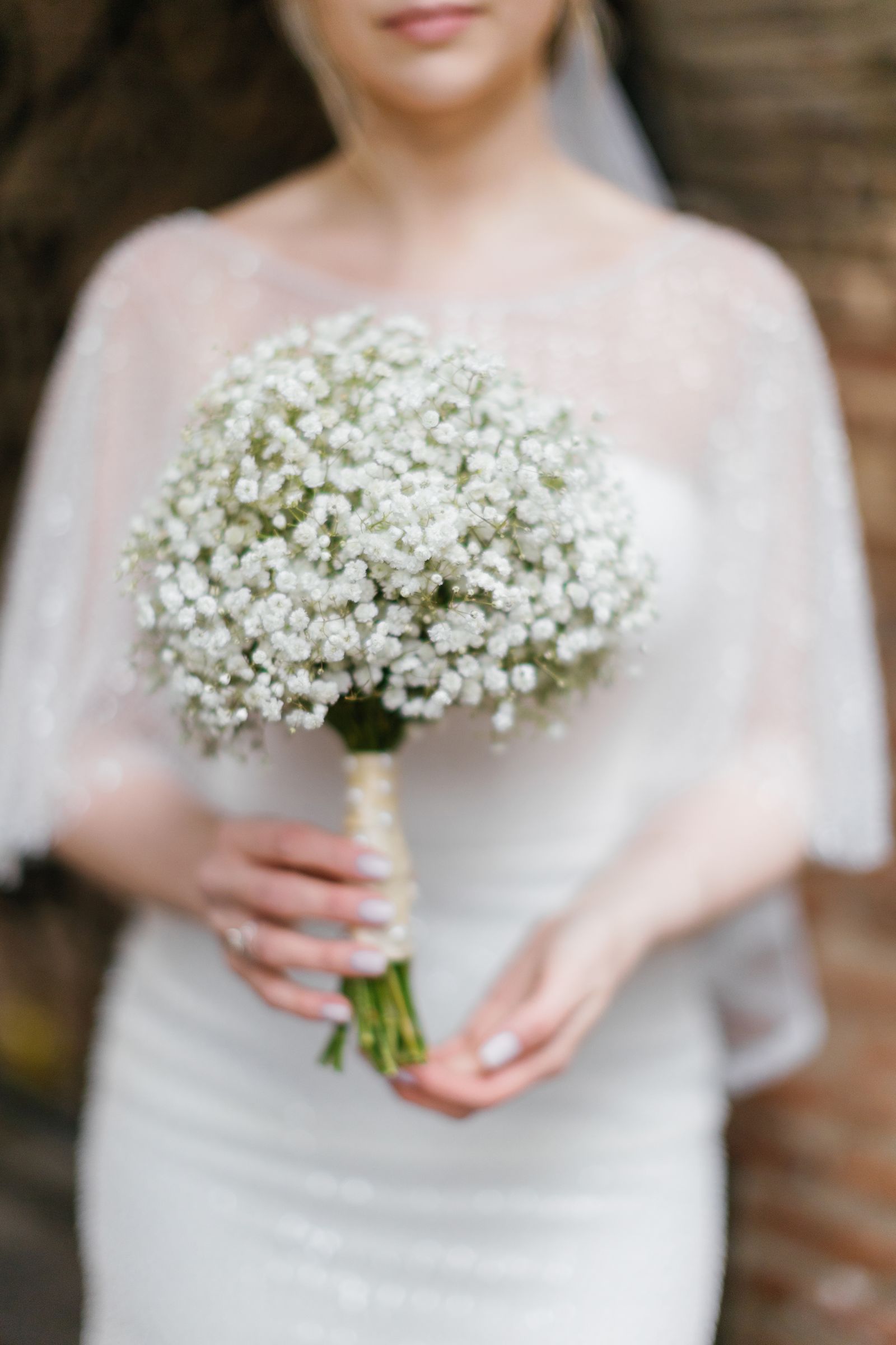 Bride in a sheer lace capelet holding a cloud of baby's breath