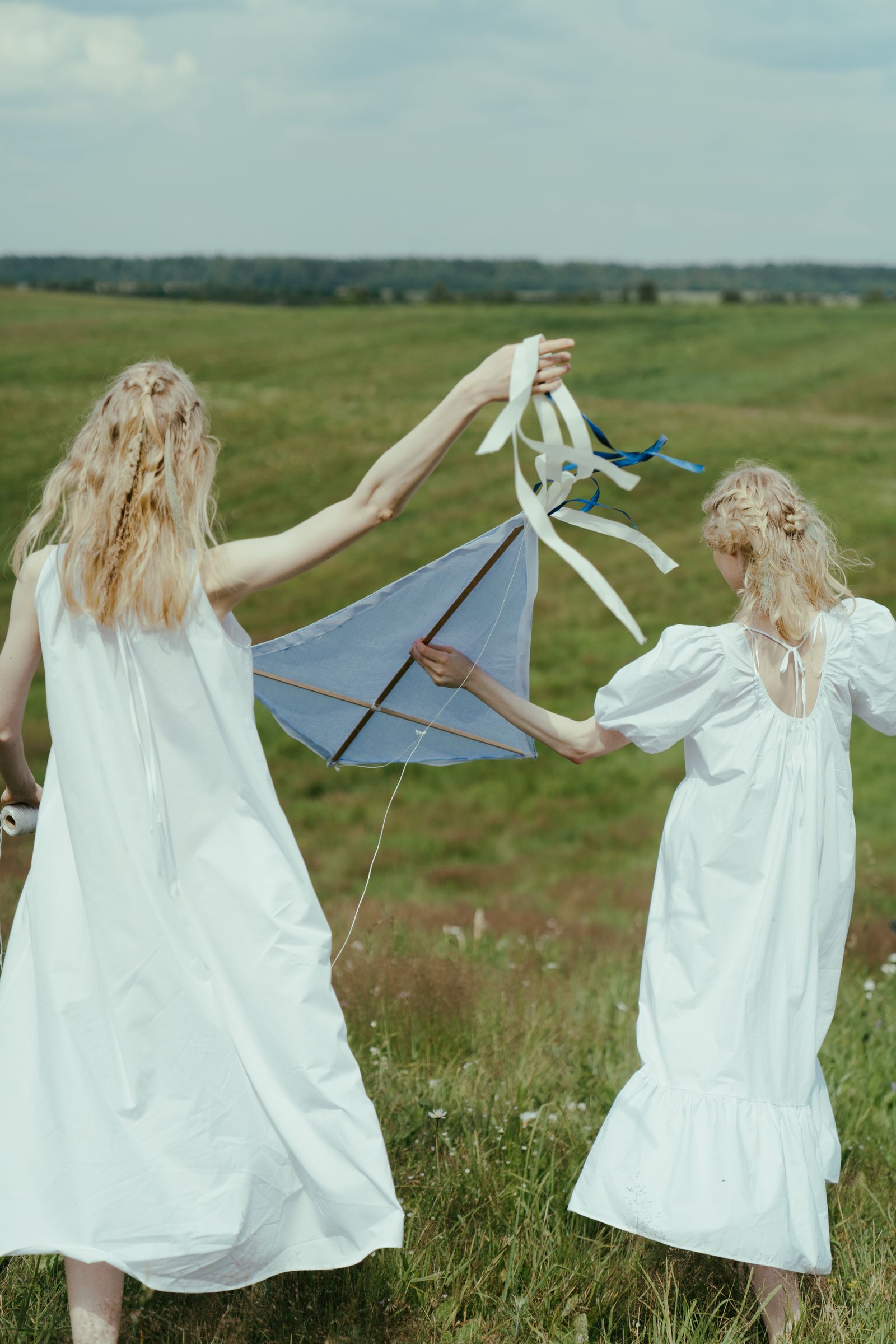 Bride and friend in white dresses playing with ribbons in a meadow