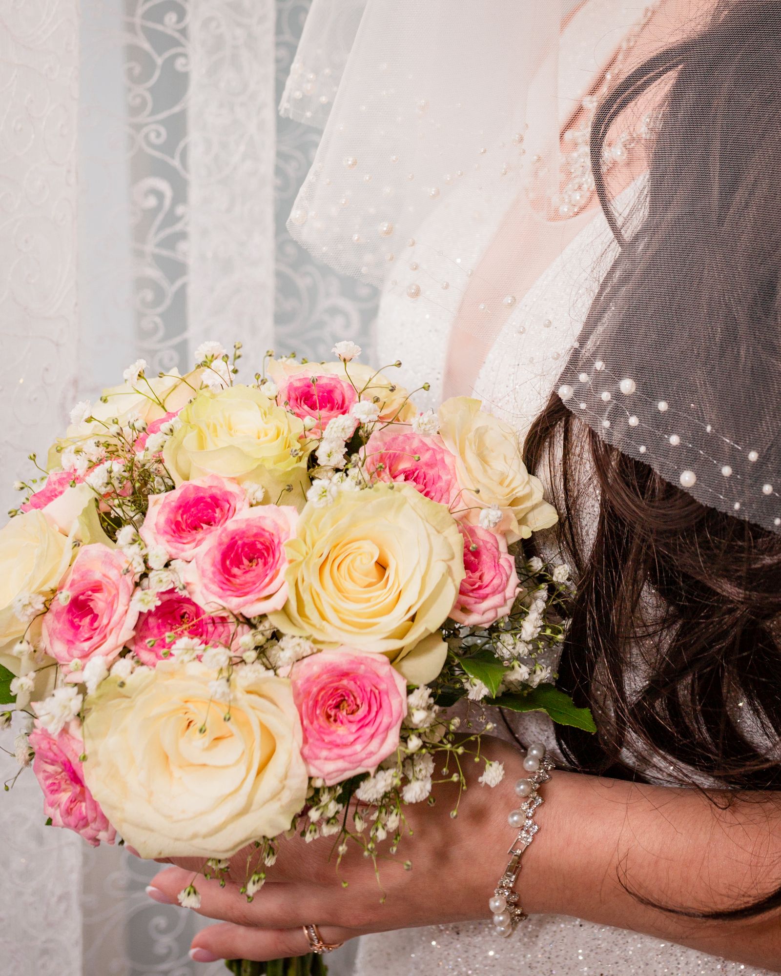 Bride holding a bouquet of blush and cream roses beside her pearl veil