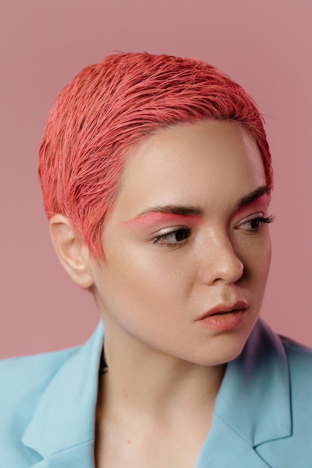 Rose-coral cropped hair against a pink backdrop
