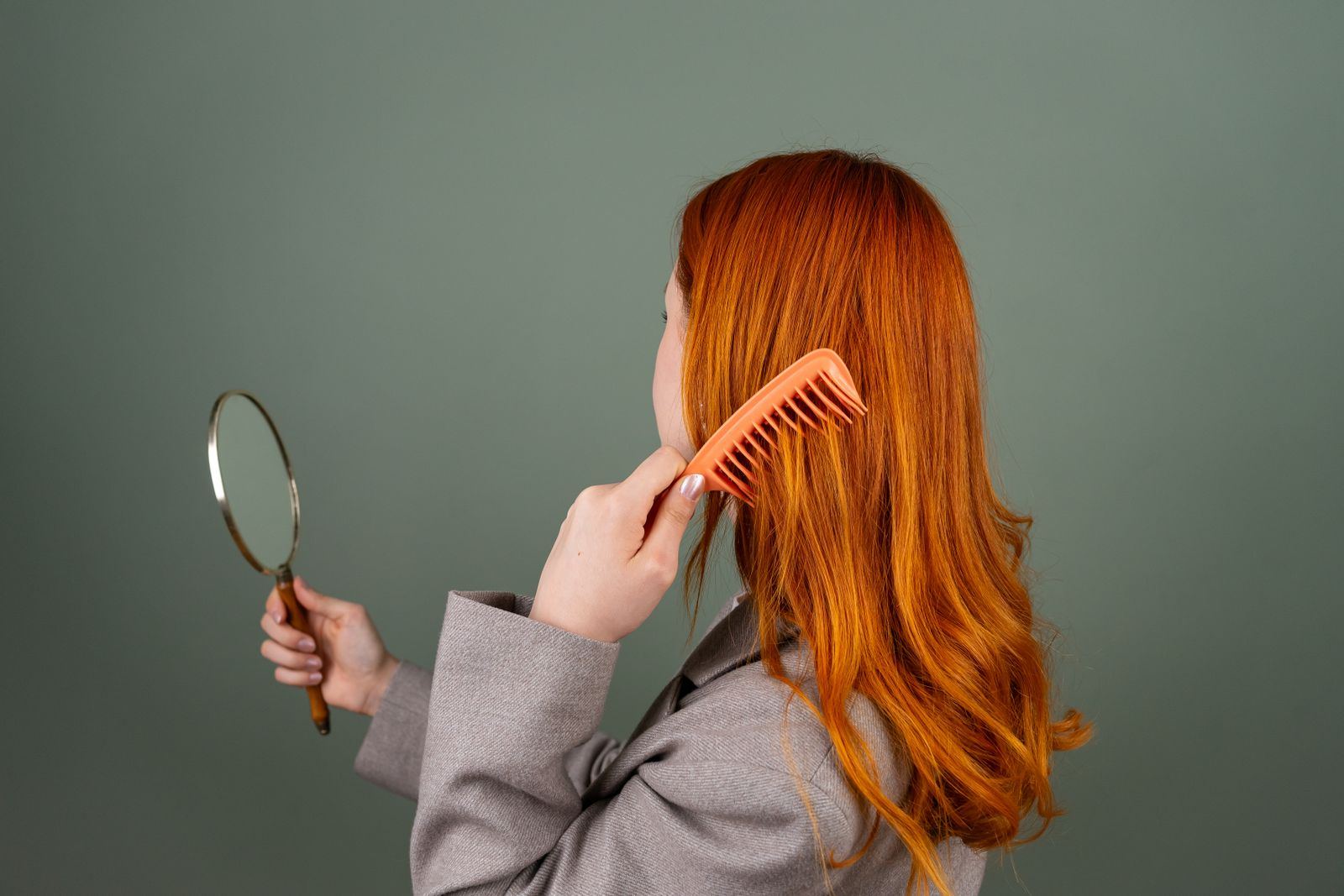 Woman with long vivid copper hair combing it while looking into a hand mirror