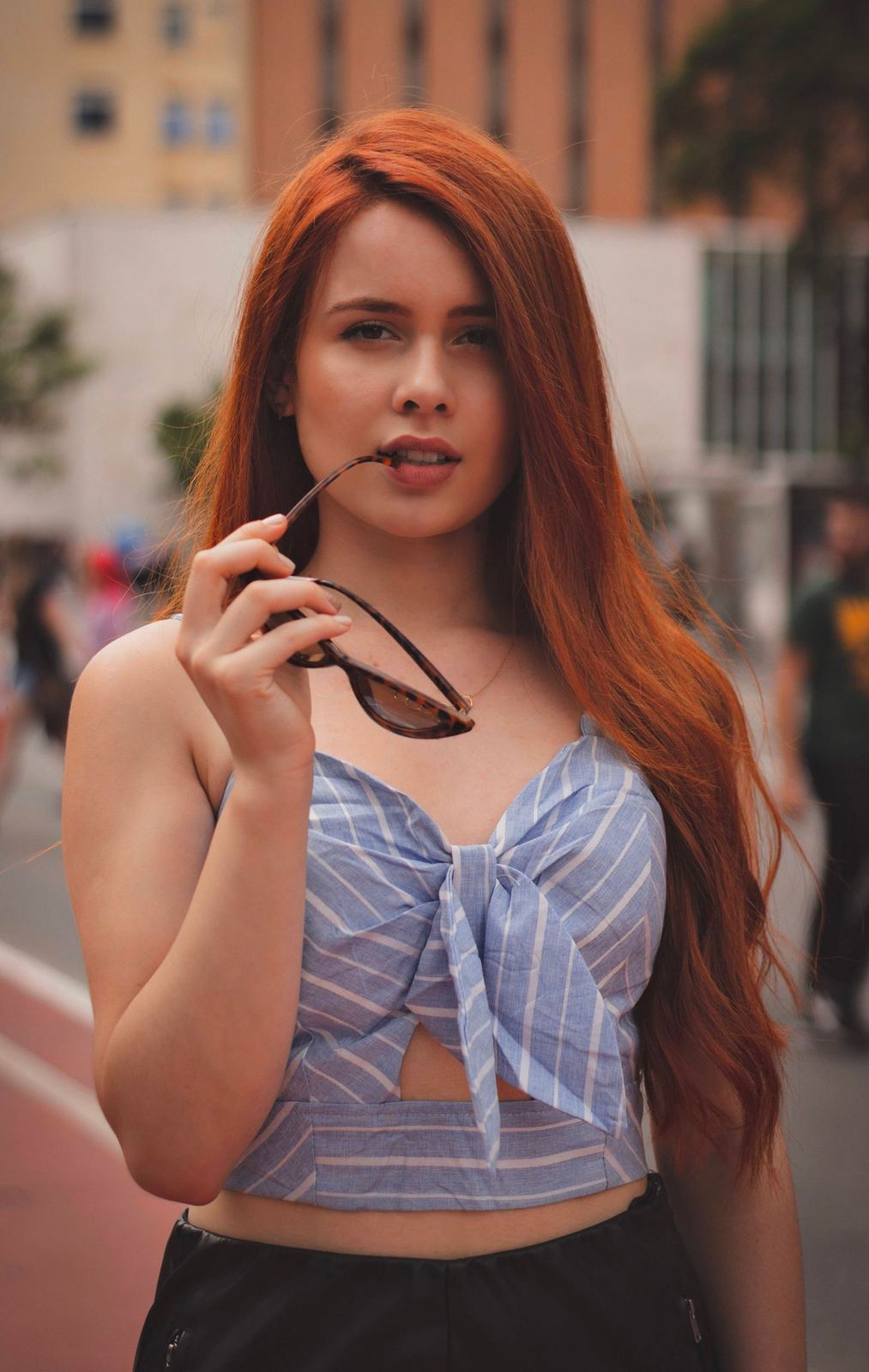 Woman with long copper-red hair holding sunglasses on a city street