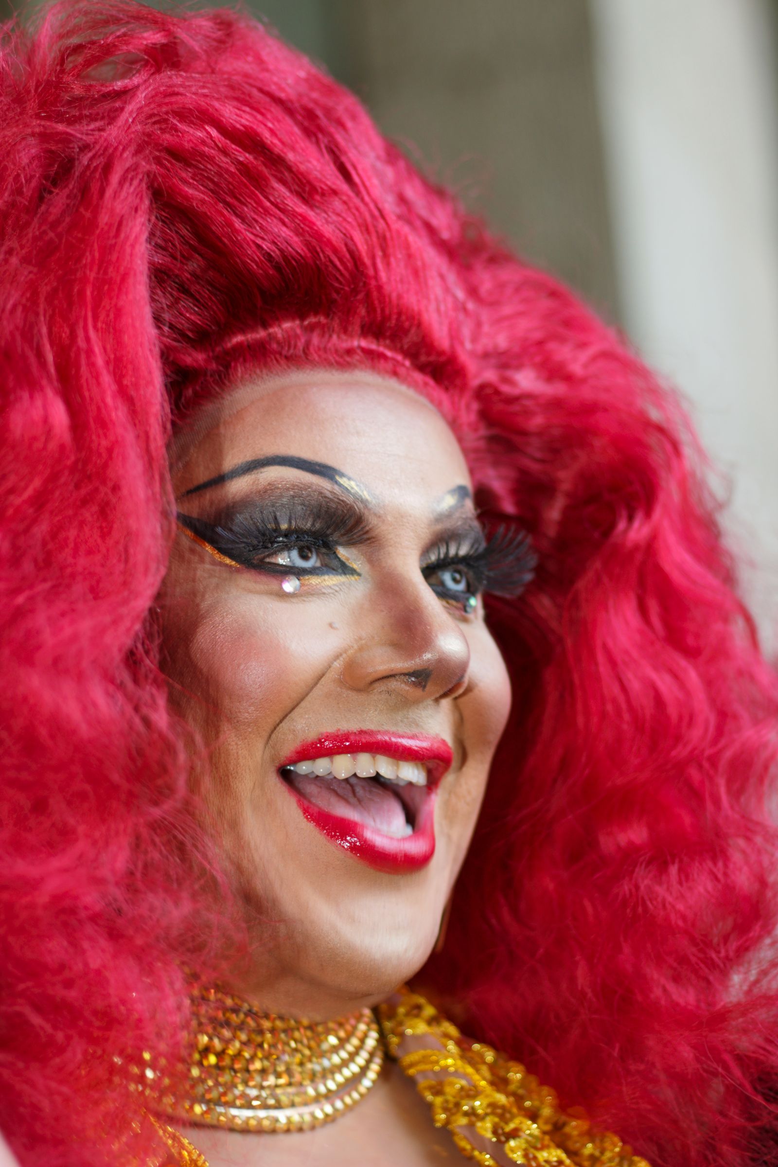 Drag performer with voluminous scarlet hair, laughing