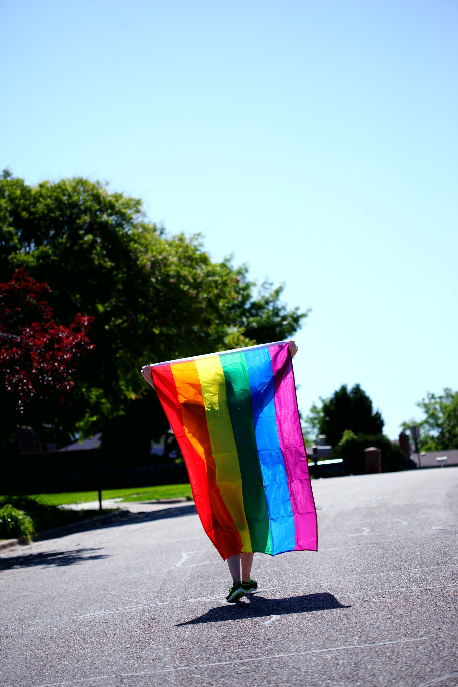 Person holding a rainbow pride flag open in a sunny street