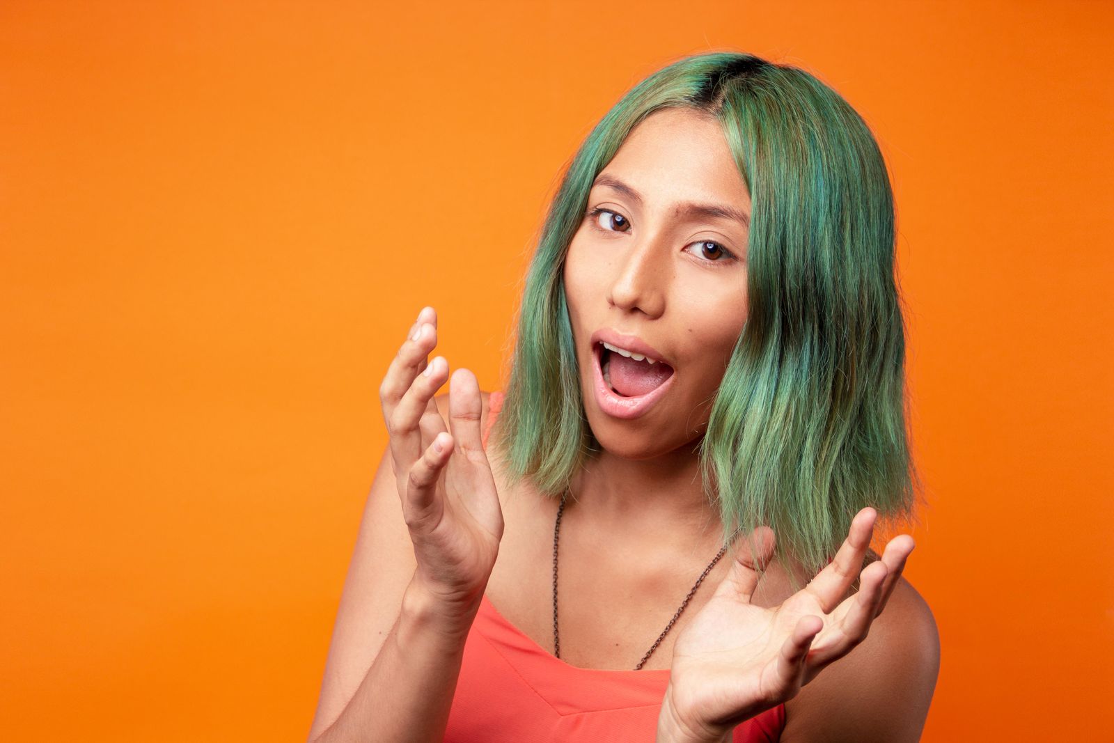 Woman with a sea-green bob laughing against an orange wall