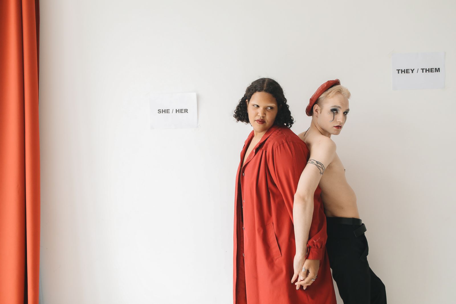 Two friends posing in front of she/her and they/them signs