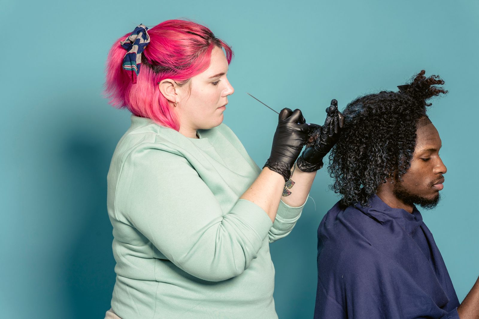 Pink-haired stylist sectioning a client’s natural coils