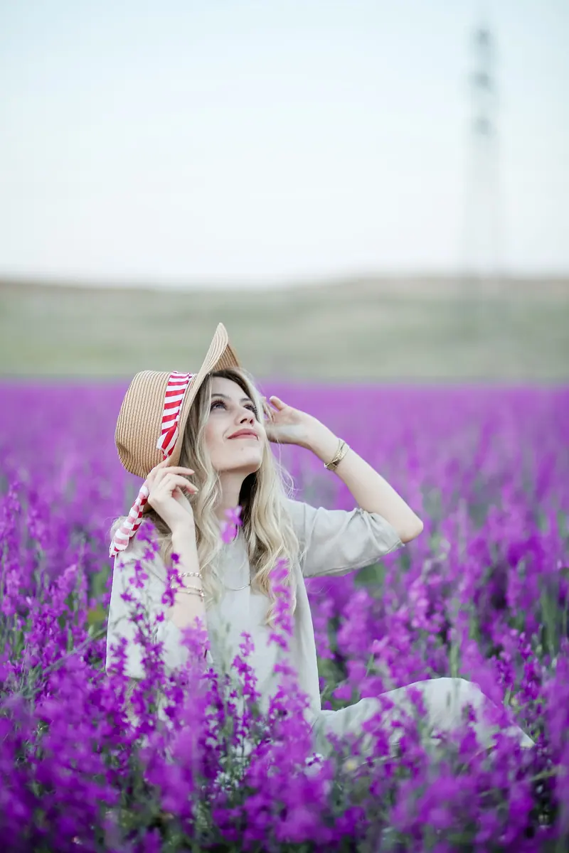 Young woman in a hat relaxing in a vibrant purple flower field, enjoying a sunny day.