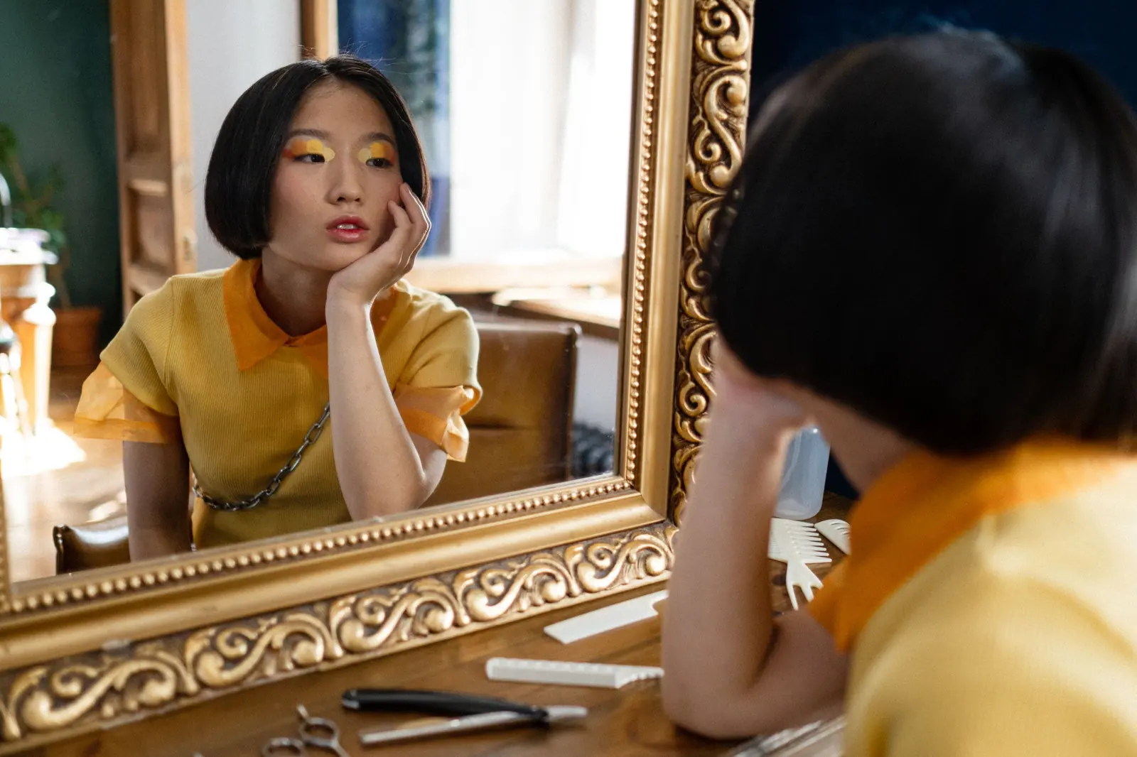A thoughtful woman gazes into a salon mirror, surrounded by hairdressing tools.
