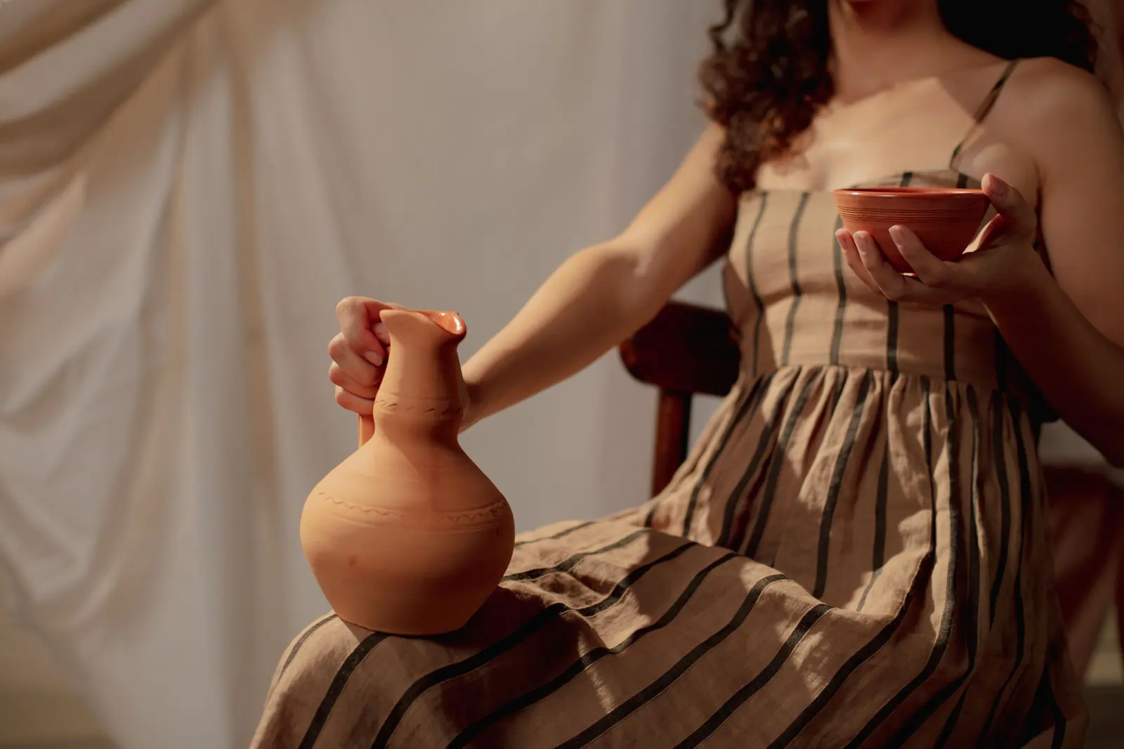 A woman in a striped dress holding a ceramic jug and bowl, creating an artistic vintage feel.