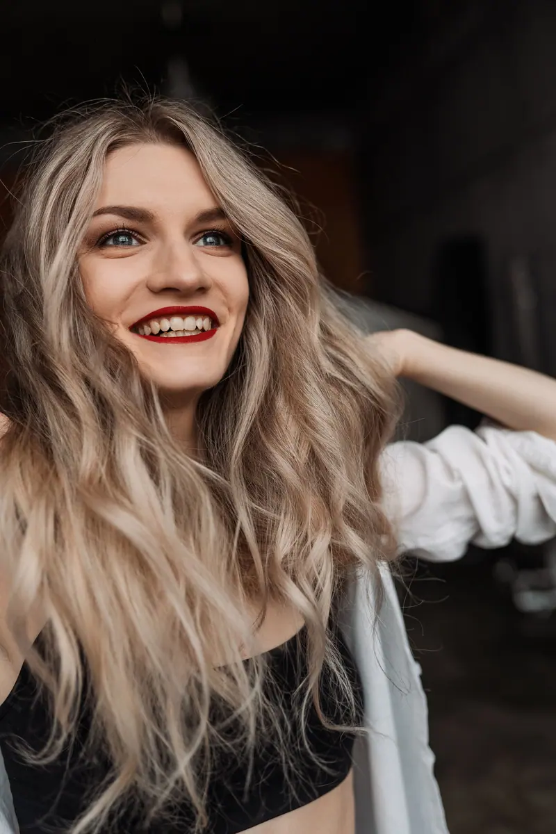 Portrait of a cheerful woman with wavy hair and red lips smiling indoors.