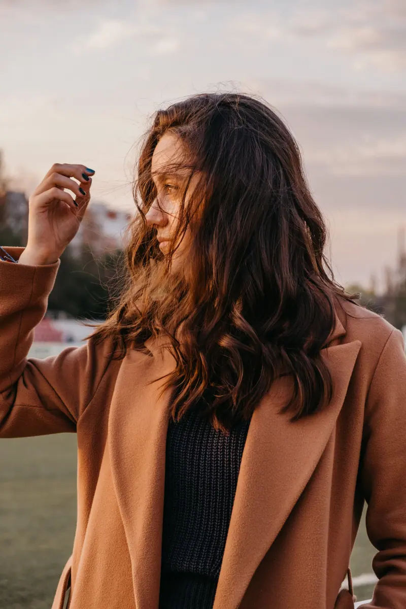 Portrait of a brunette woman in a coat with flowing hair at sunset outdoors.