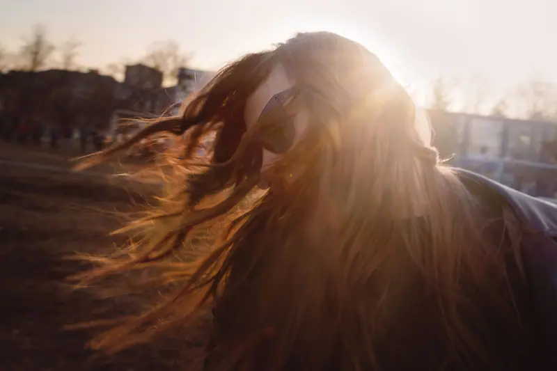 Woman flipping hair outdoors in sunlight, wearing sunglasses for style and protection.