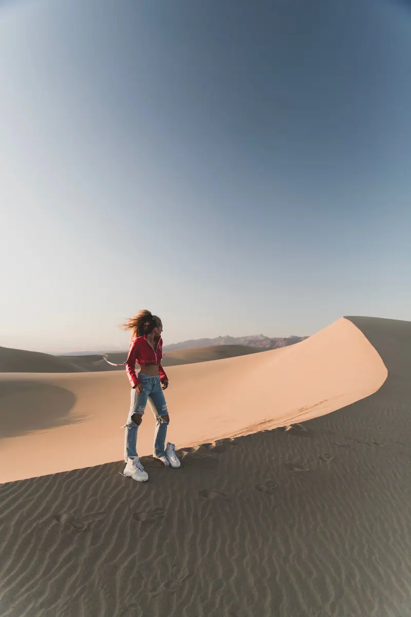 A woman stands on a sunlit sand dune in the desert, capturing a serene and adventurous moment.