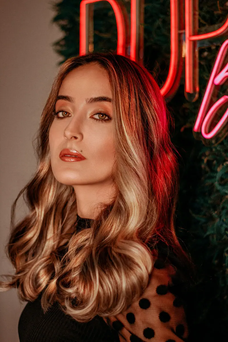 Elegant woman with wavy hair and red neon accents, exuding modern style.