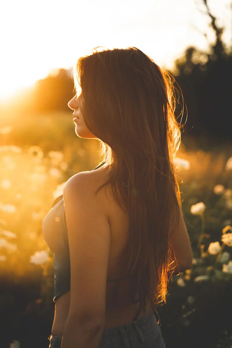 A side view portrait of a woman during golden hour in a sunlit field with sunflowers.