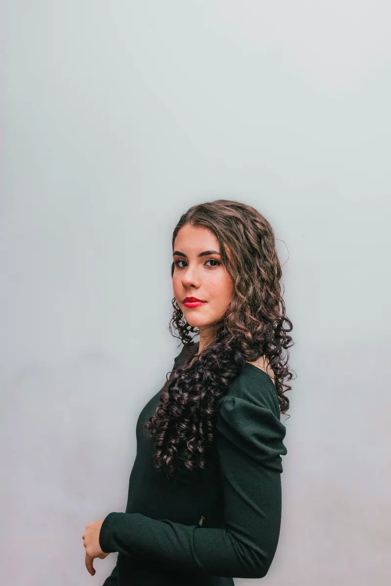 Stylish portrait of a young woman with curly hair and green dress on a neutral background.