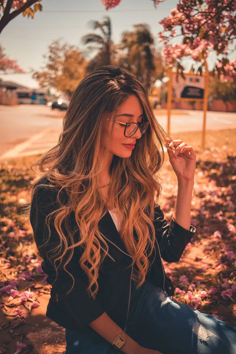 Woman with wavy hair and eyeglasses in a stylish outdoor autumn scene under falling leaves.