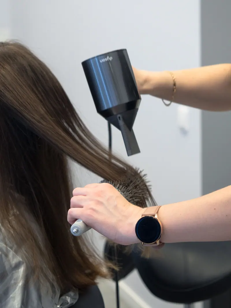 Close-up of a hairdresser using a hairdryer and brush for styling in a salon.
