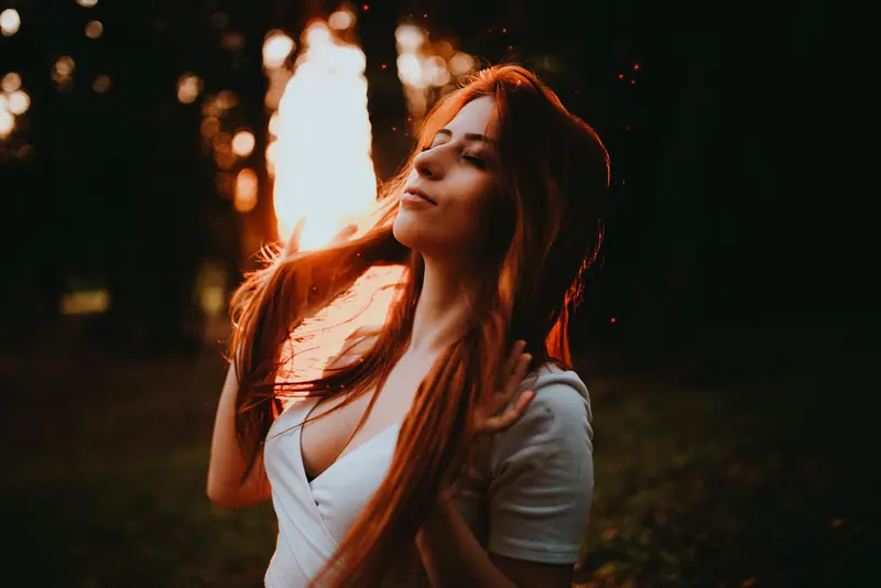 A serene young woman with red hair enjoys a peaceful moment in the sunset outdoors.