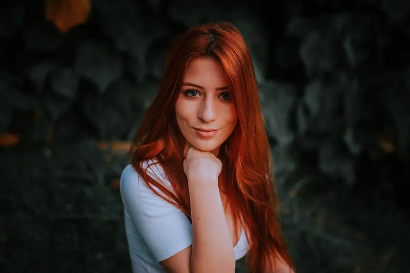 Captivating portrait of a smiling redhead woman outdoors, surrounded by greenery.