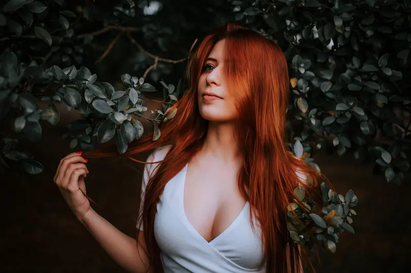 Close-up portrait of a red-haired woman surrounded by greenery, embodying natural beauty.