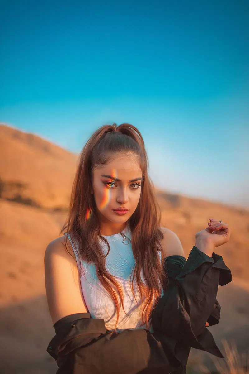 Portrait of a young woman in a desert landscape with rainbow light effect on her face.