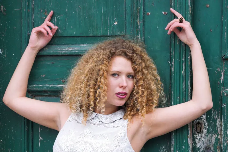 Caucasian woman with curly hair posing against a weathered green door, creating a striking contrast.