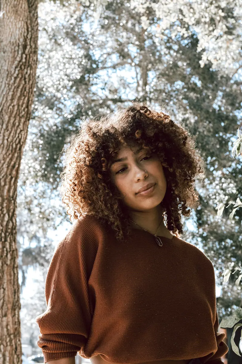 Stylish woman with curly hair wearing a brown sweater outdoors.