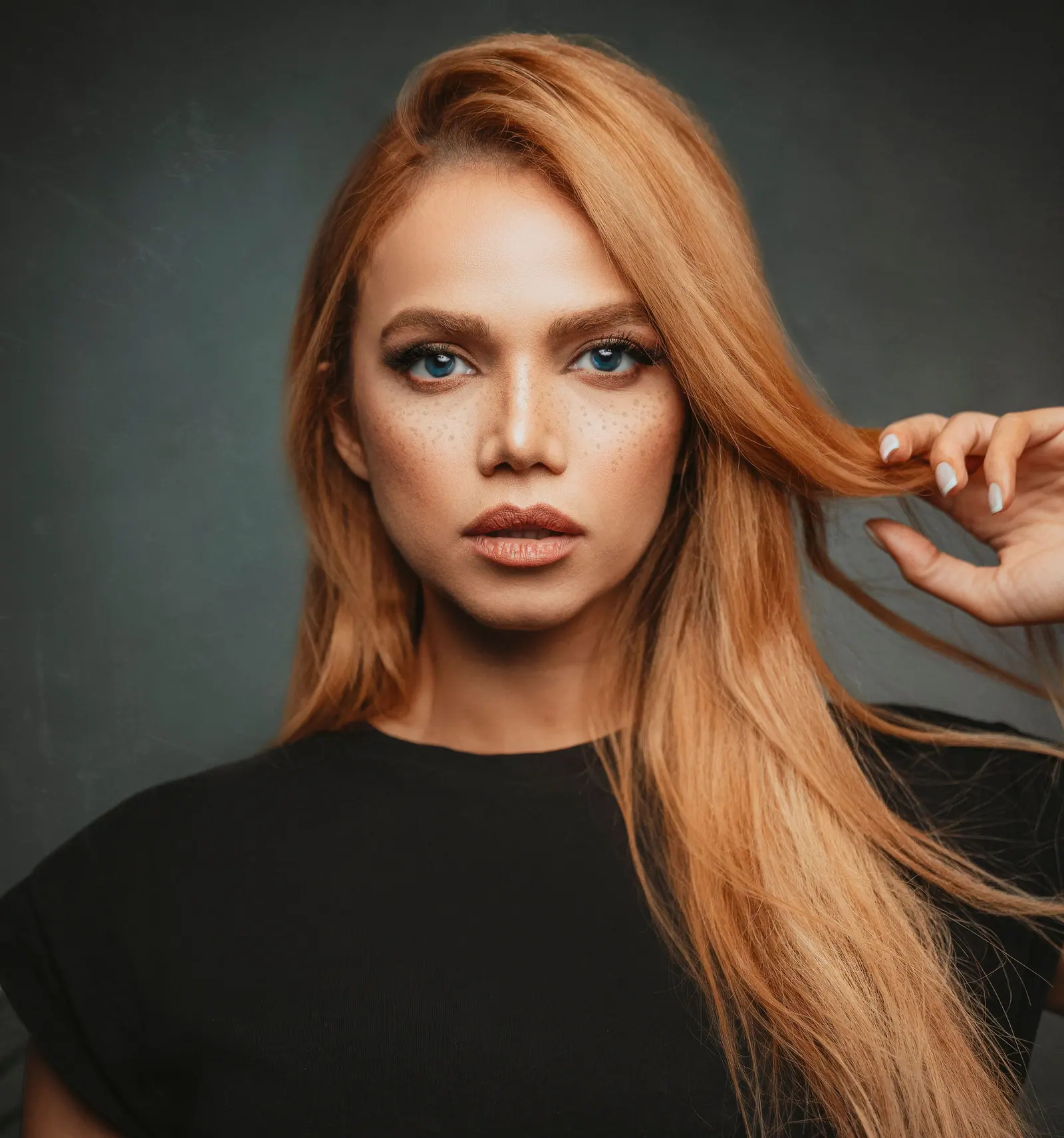 Close-up portrait of a woman with blonde hair and freckles against a gray studio background.