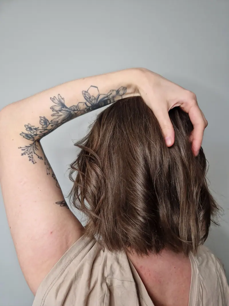 Back view of woman with floral arm tattoo and mid-length brown hair in a neutral tone.