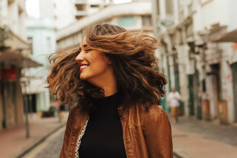Joyful woman with flowing hair spinning on a city street, exuding happiness.