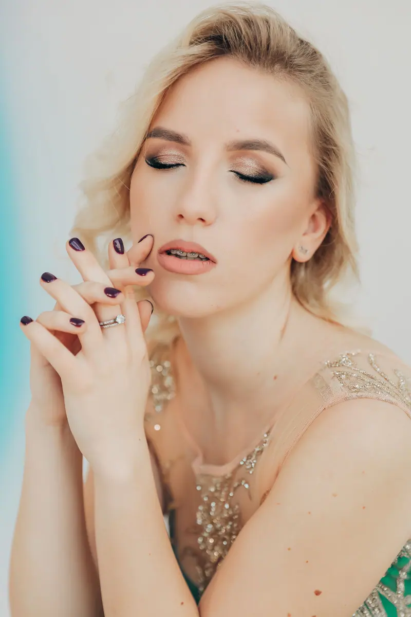 A beautiful blonde woman with closed eyes and painted nails in an elegant pose indoors.
