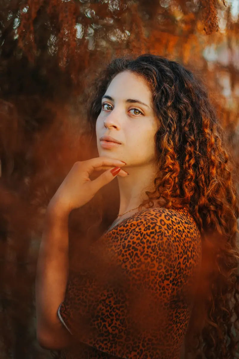A captivating portrait of a woman with curly hair in a leopard print top set against a warm, autumnal background.