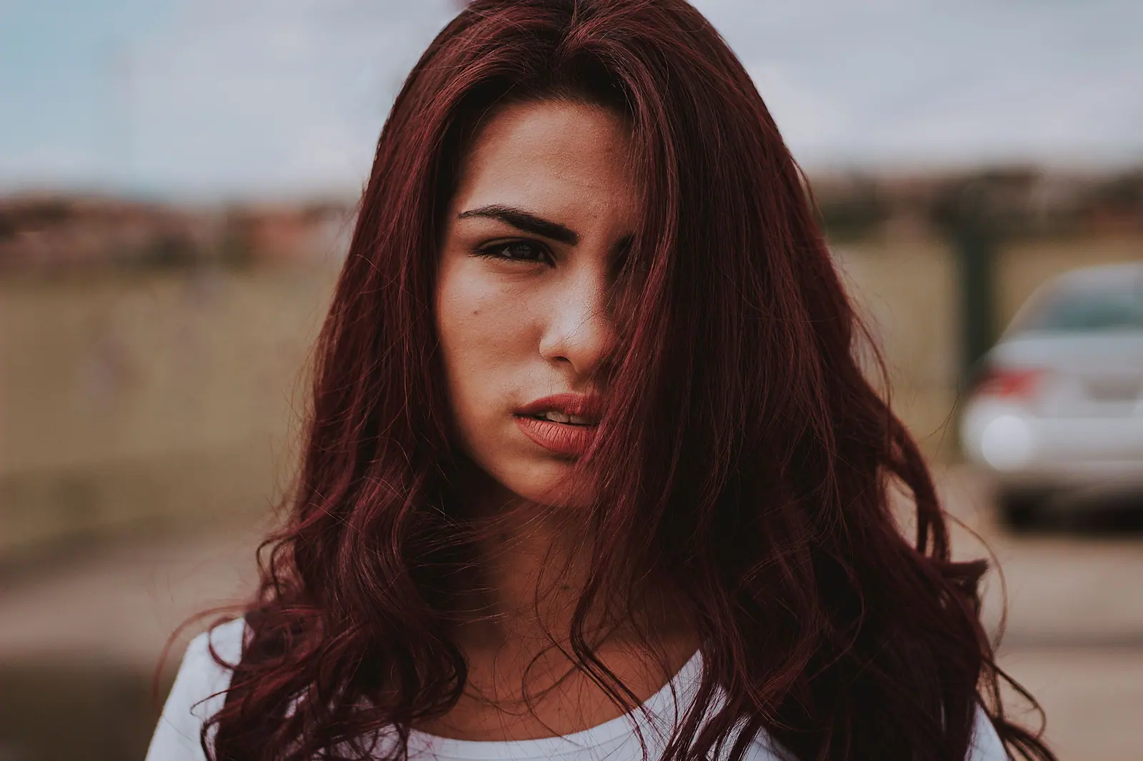 Woman with long wine-red waves looking into the camera on a quiet street