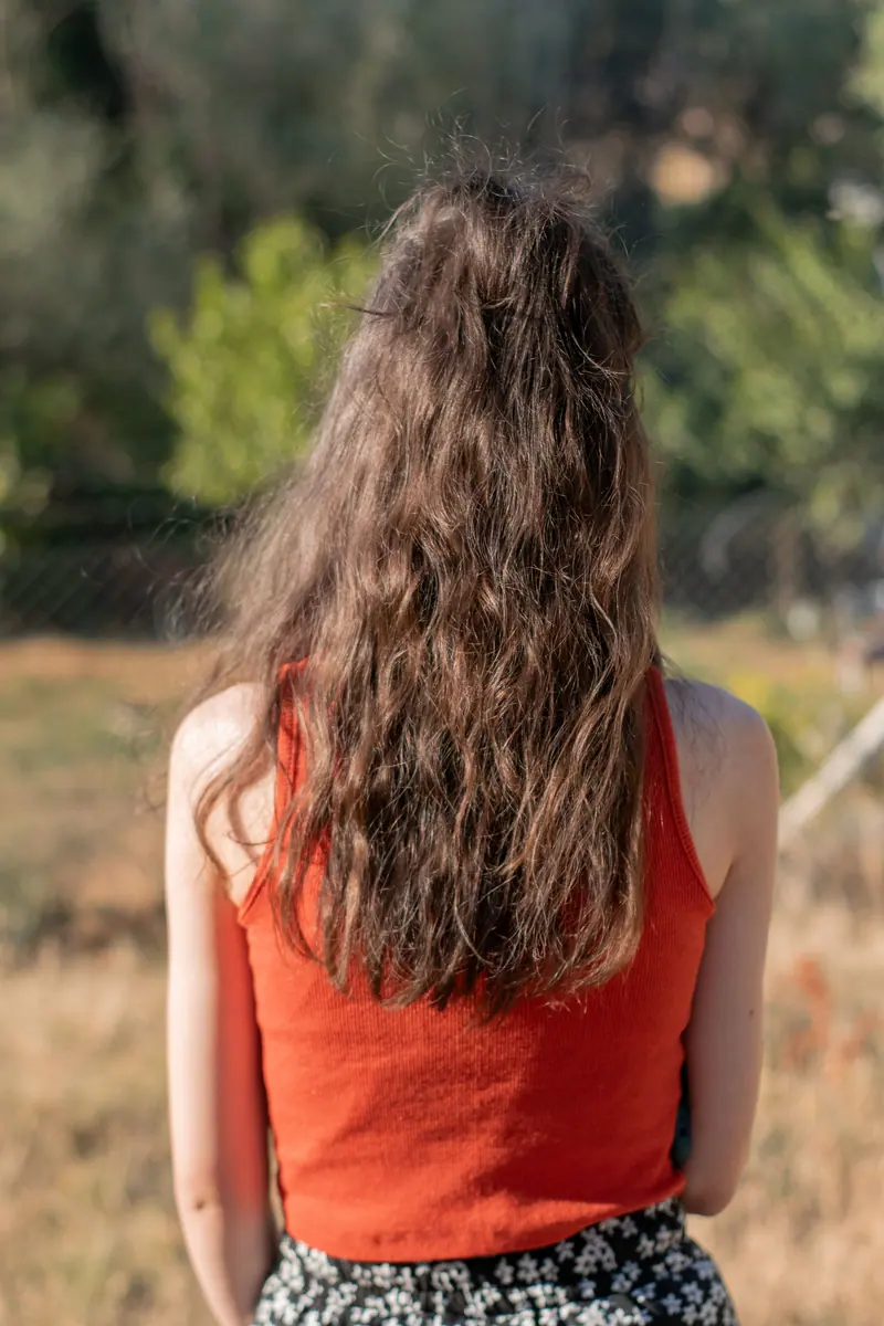 Back view of a woman with long wavy hair wearing a red tank top in a sunny field.