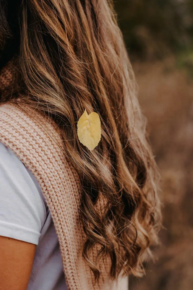 Close-up of a woman's hair with a yellow leaf, capturing the essence of fall.