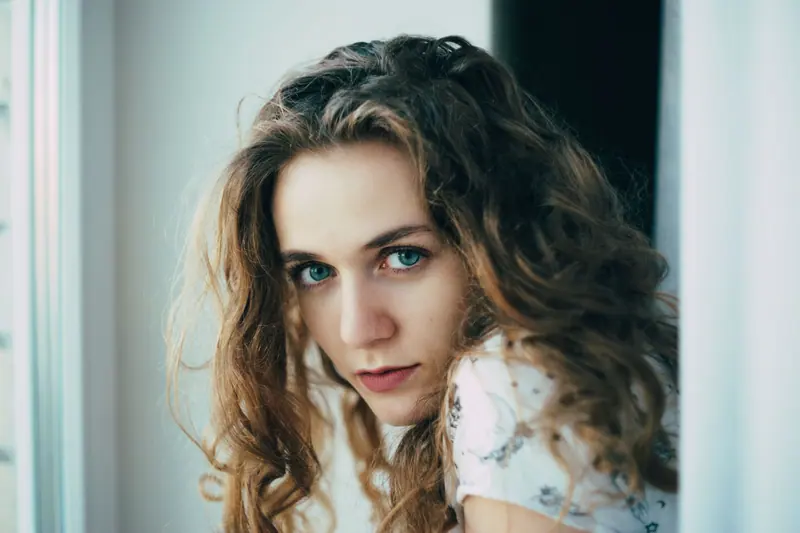 Close-up portrait of a woman with wavy brown hair gazing softly.