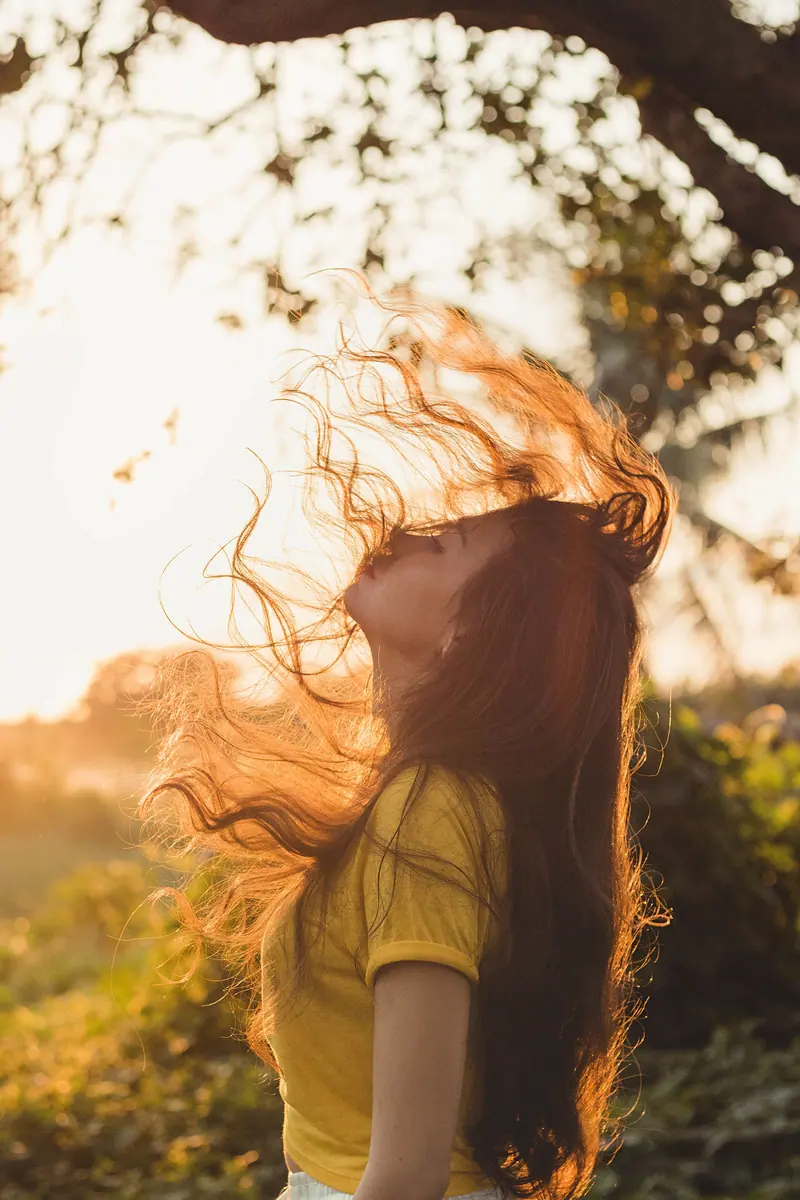 Artistic portrait of a woman with flowing hair against a sunset backdrop, capturing a moment of freedom and serenity.