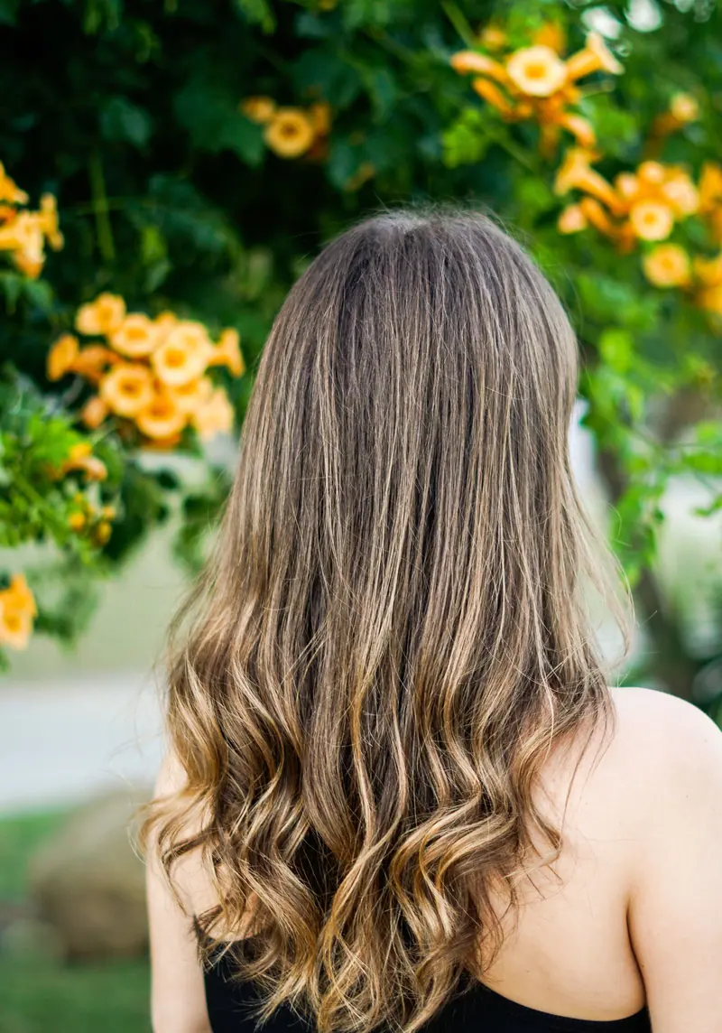 A woman with long hair stands in a garden with vibrant yellow flowers, serene and elegant.