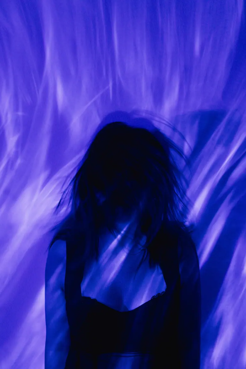 Striking portrait of a woman silhouetted against blue swirling lights, creating a surreal, dreamy atmosphere.